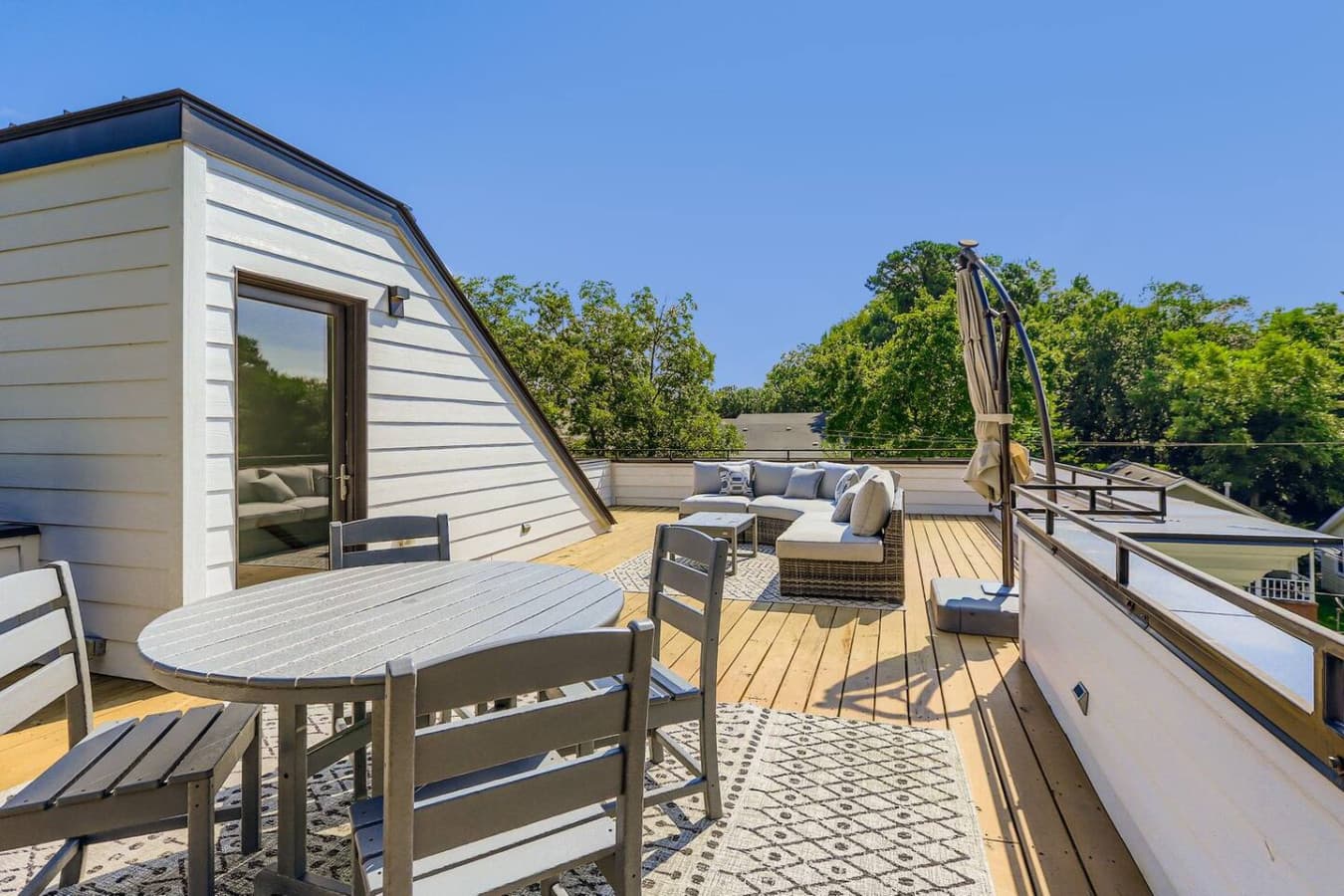 Unit A: Escape to this private rooftop retreat nestled among the trees, featuring a cozy sectional sofa, umbrella-shaded lounge area, and stylish dining setup for six.