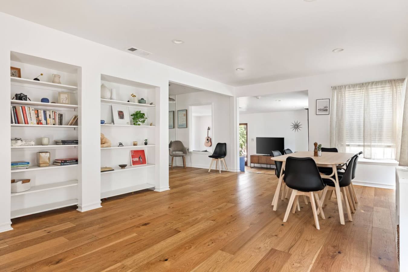 Open concept living and dining space with warm hardwood floors and built in shelving.