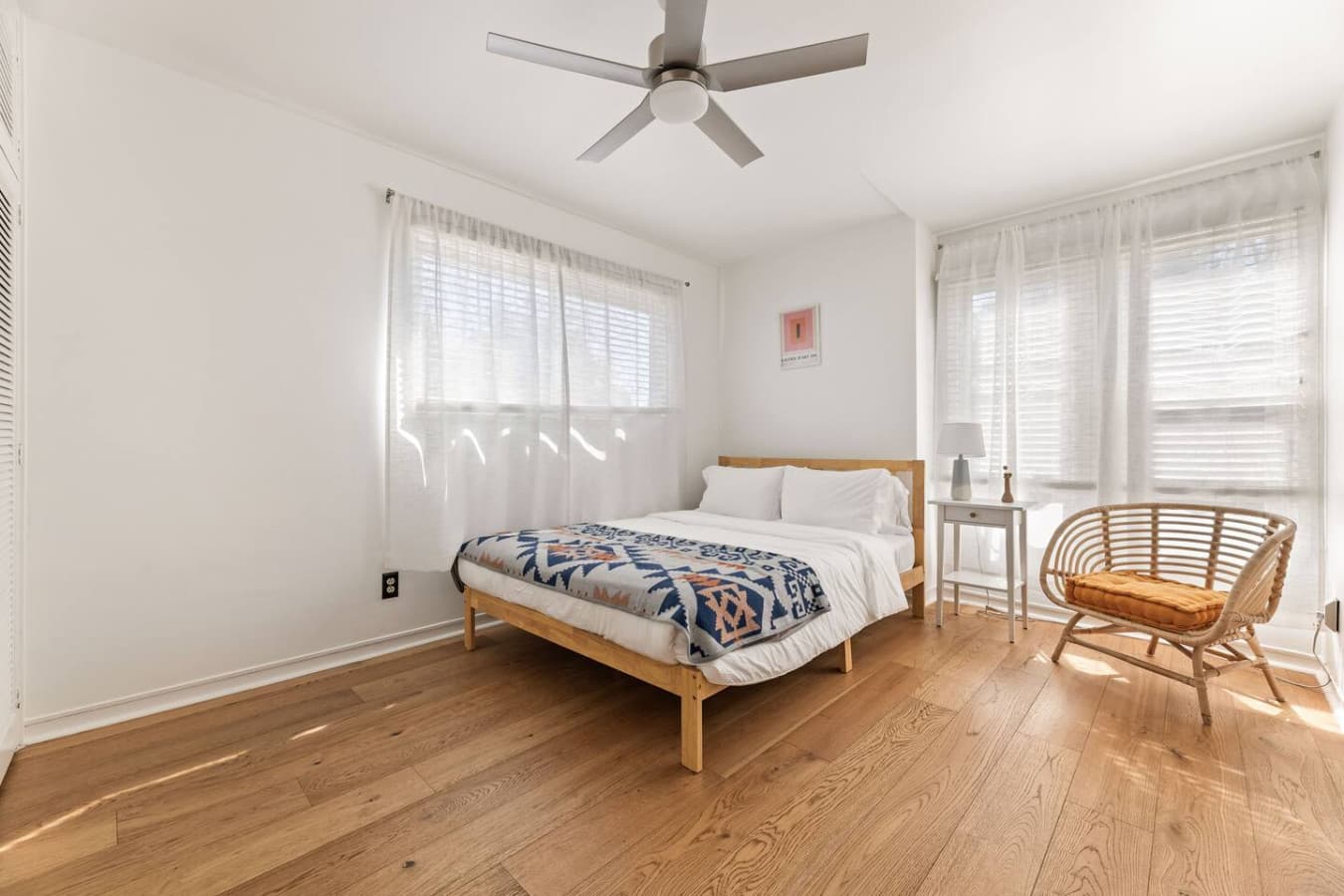 Bright bedroom with large windows, soft natural light, and warm hardwood floors.