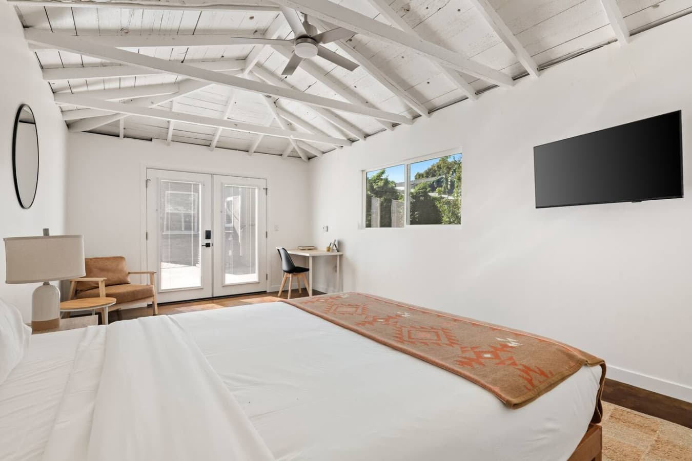 Airy bedroom with vaulted ceiling, exposed beams, and peaceful backyard views.