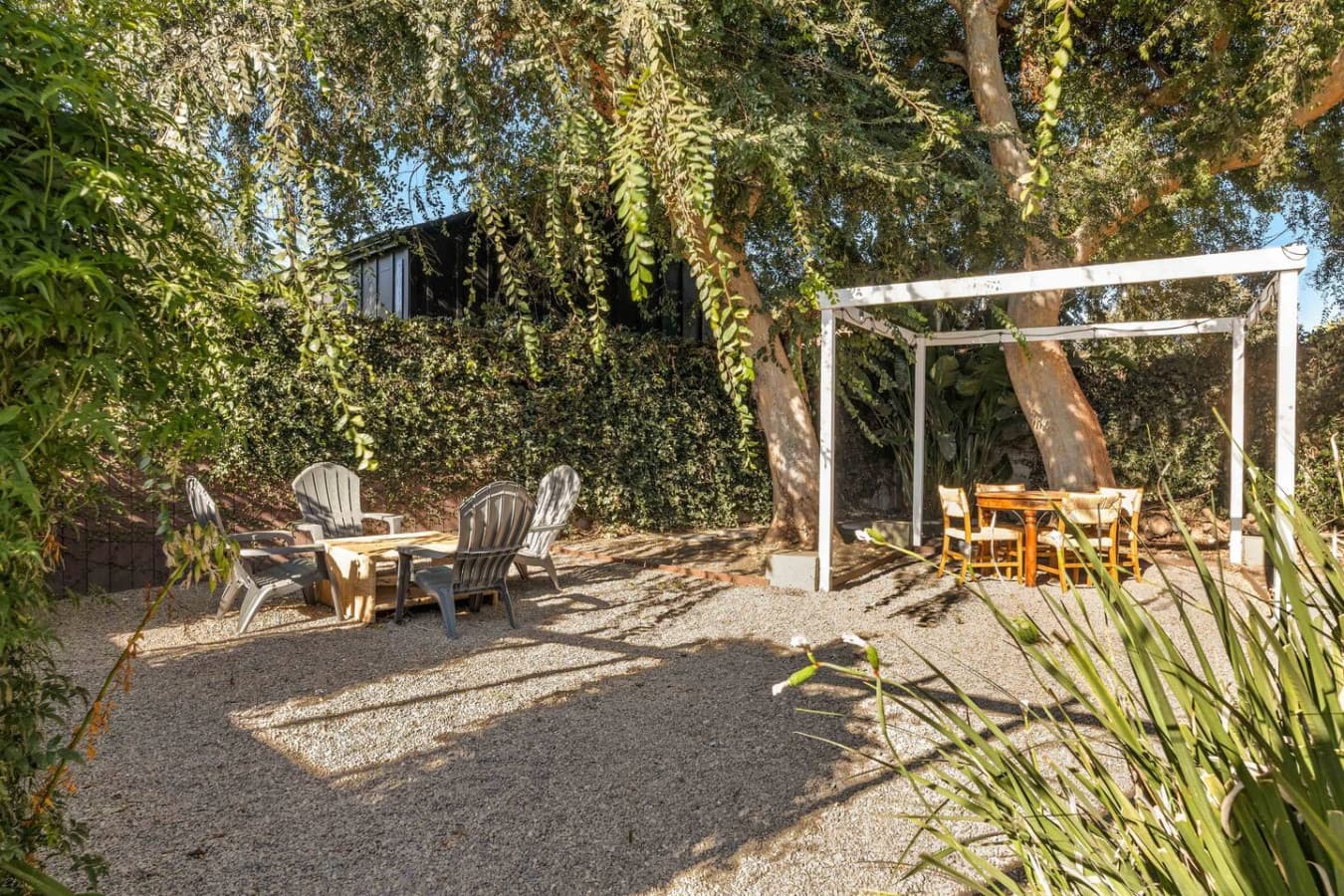 Shaded outdoor lounge space surrounded by mature trees and lush greenery.