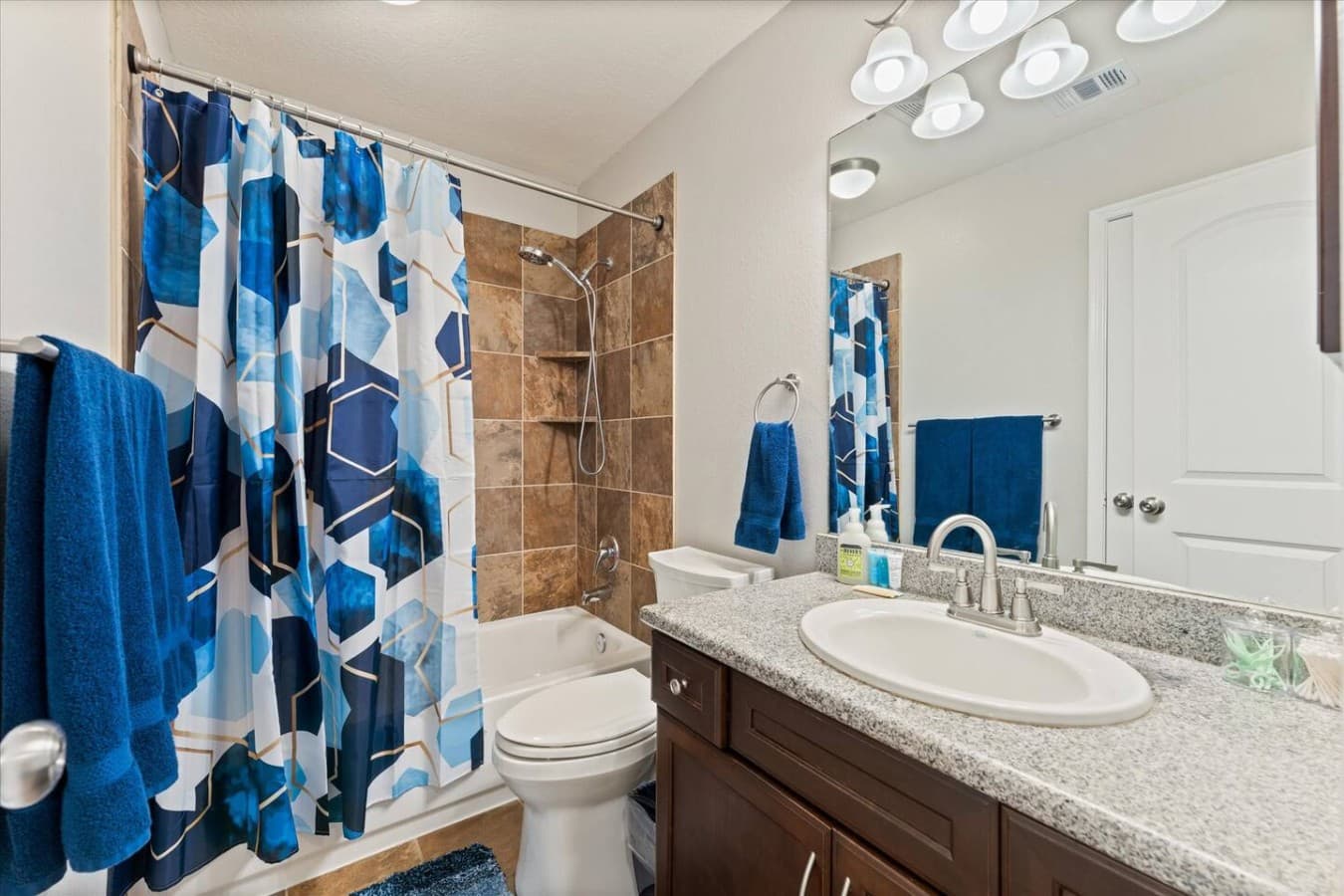 Bright guest bathroom with granite countertops, modern fixtures, and a full shower and tub combination.