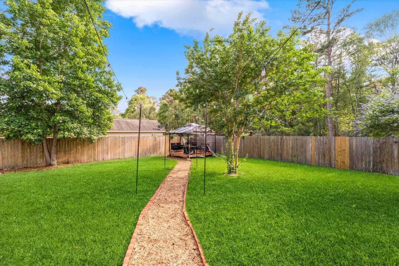 Large fully fenced backyard with a walking path leading to a cozy outdoor lounge area.