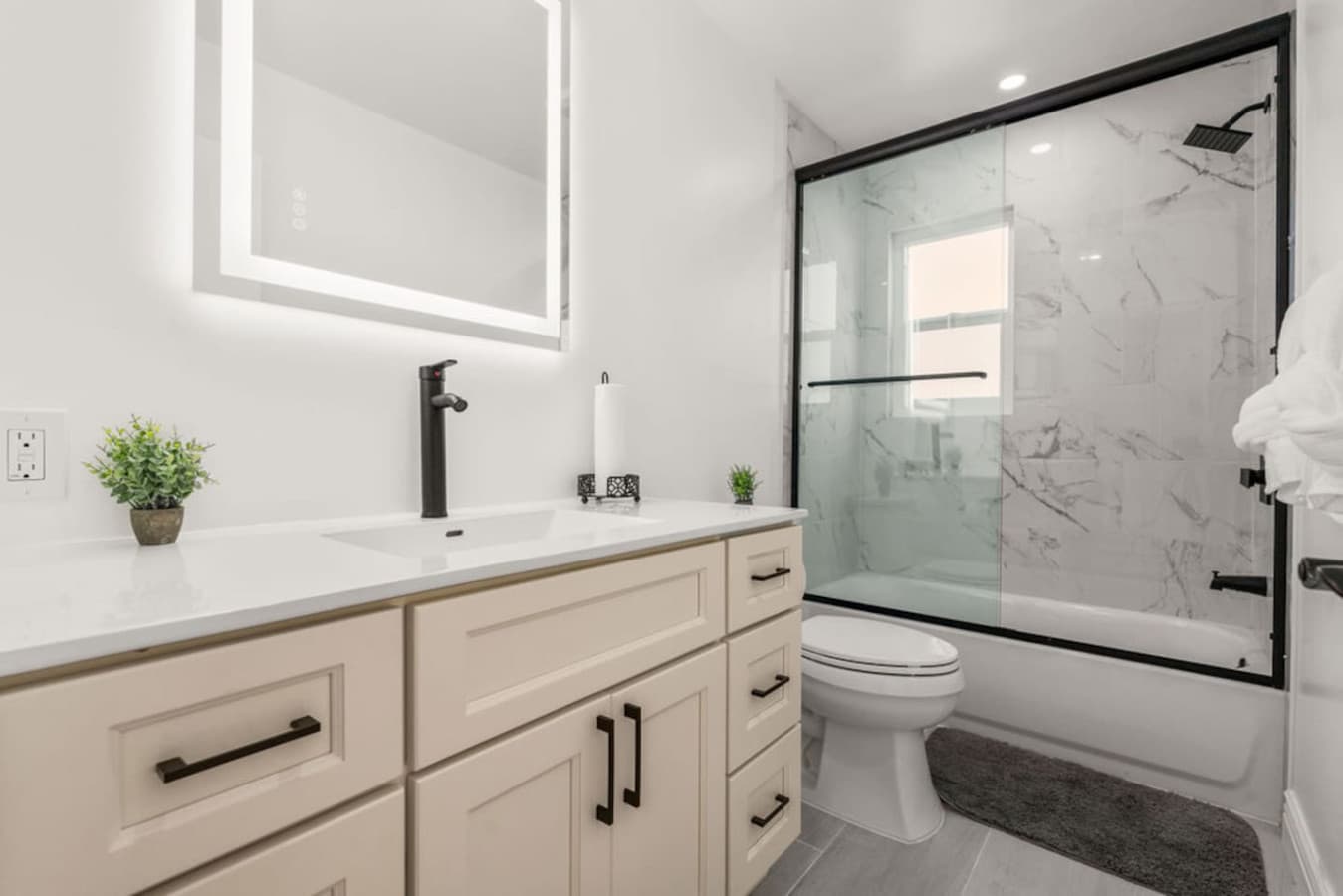 Bright modern bathroom featuring a large vanity with ample storage and a sleek glass enclosed shower and tub.