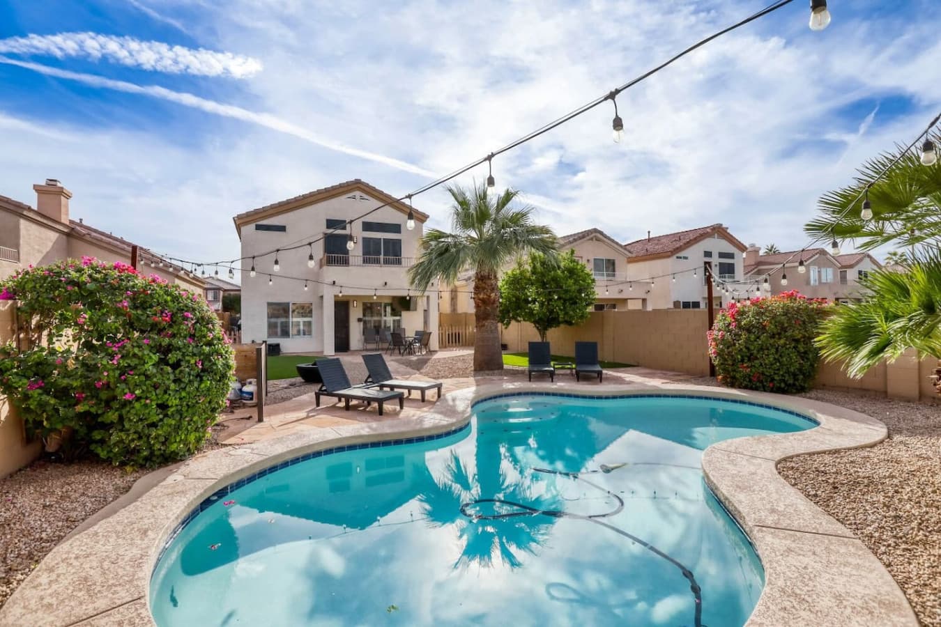 Resort style backyard with a sparkling pool and lounge seating under open skies.