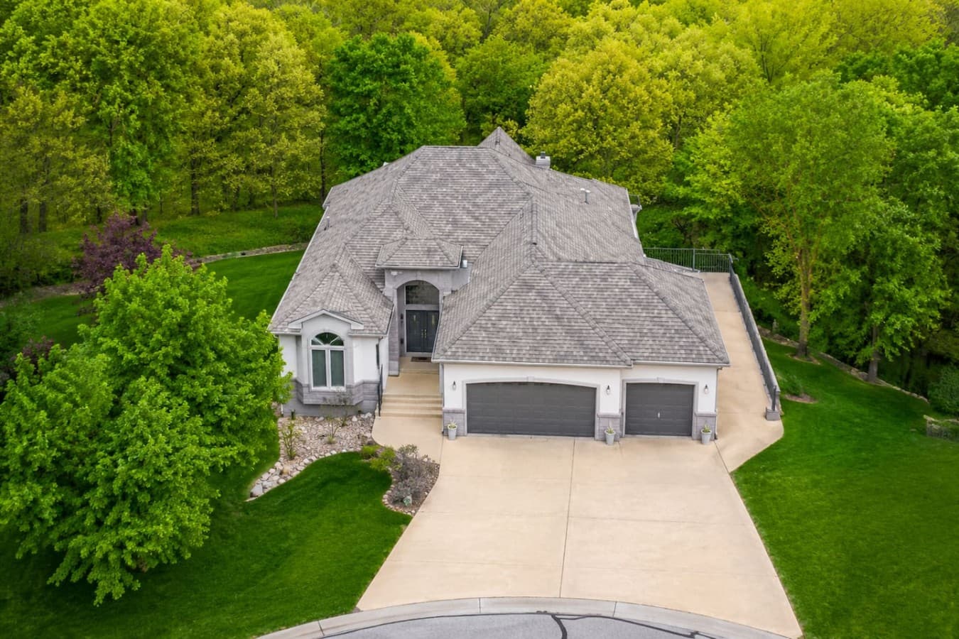 Stunning exterior with a grand entrance, spacious driveway, and surrounded by peaceful wooded scenery.
