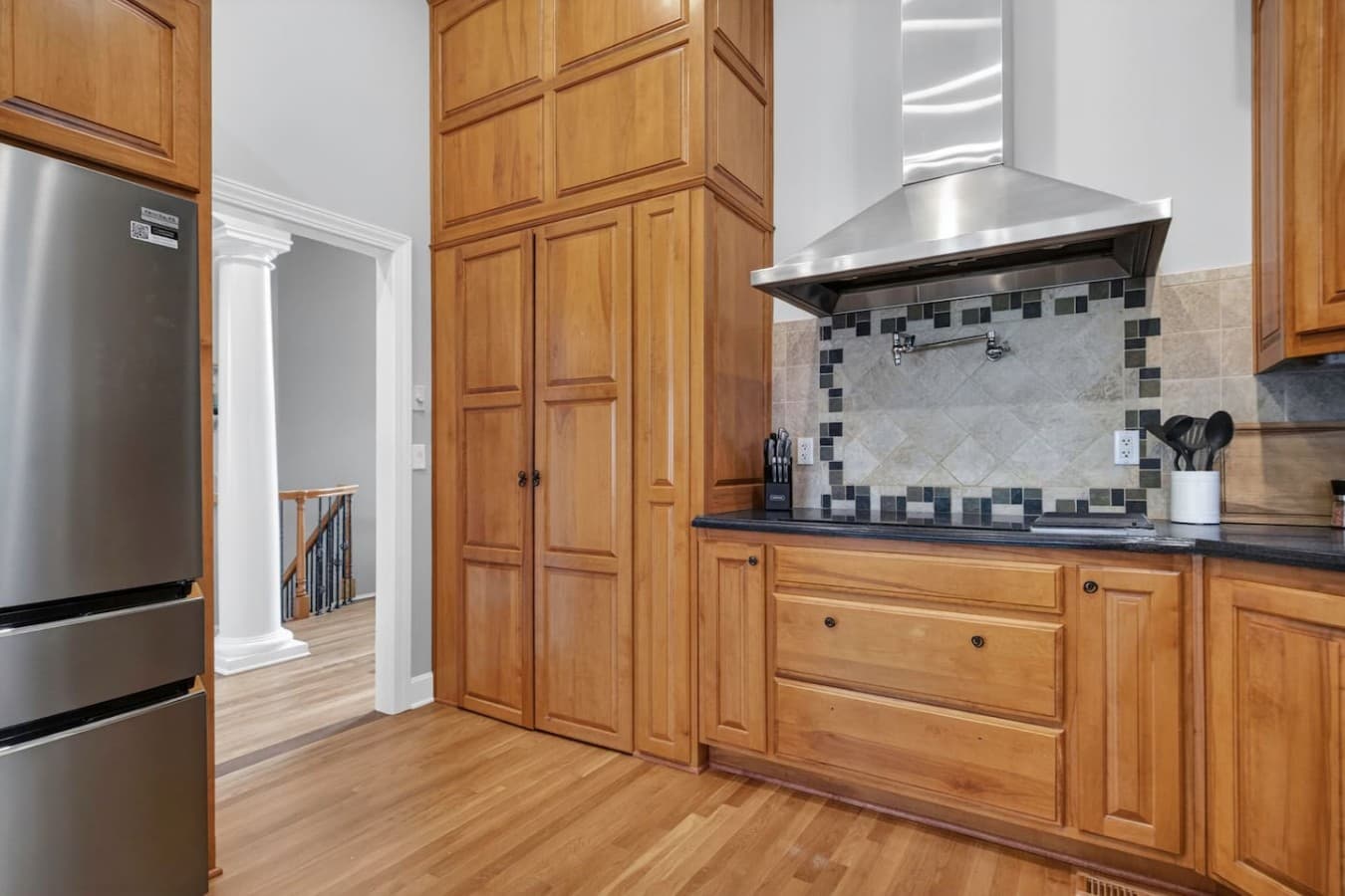 Spacious kitchen featuring double height cabinetry, sleek range hood, and warm hardwood floors.