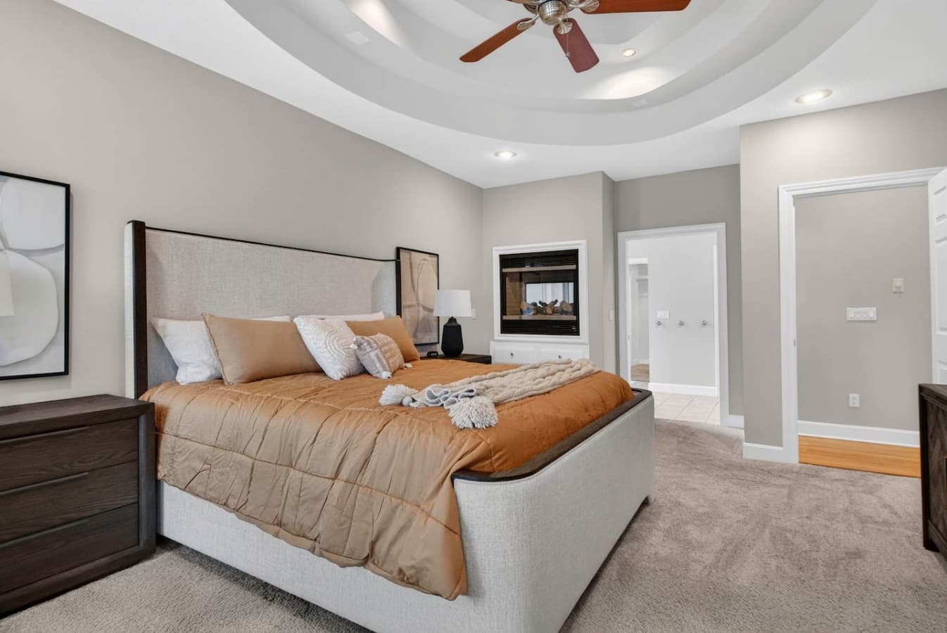 Spacious primary bedroom with tray ceilings, plush carpeting, and a cozy in room fireplace.
