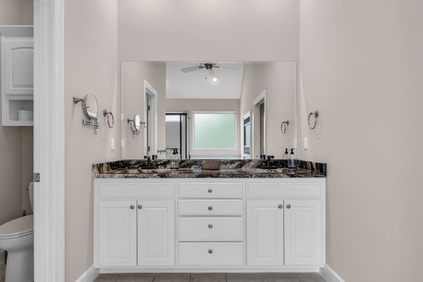 Spacious primary bathroom with dual vanities, granite countertops, and bright natural light.
