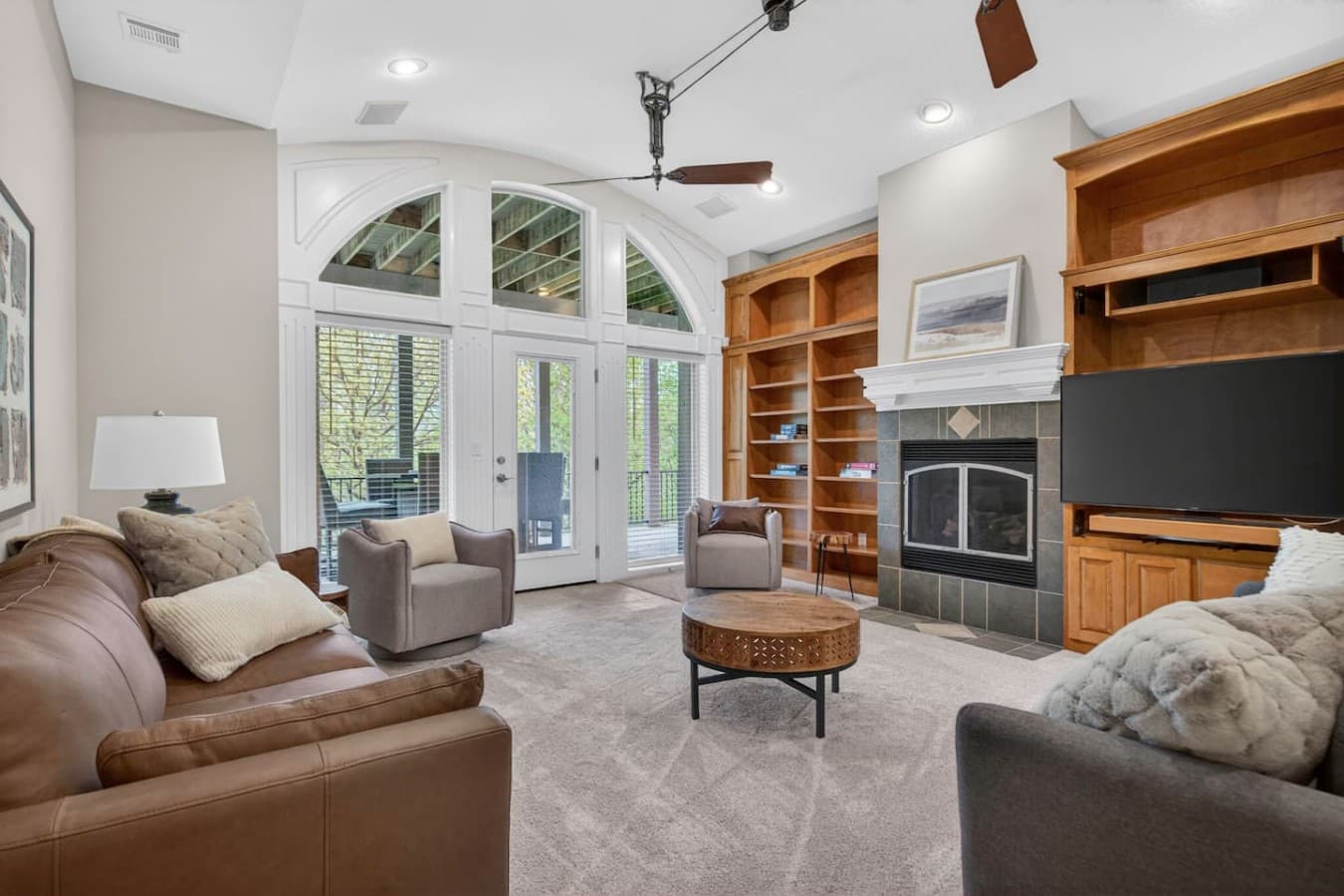 Inviting living room with fireplace, custom shelving, and oversized windows overlooking the outdoor space.