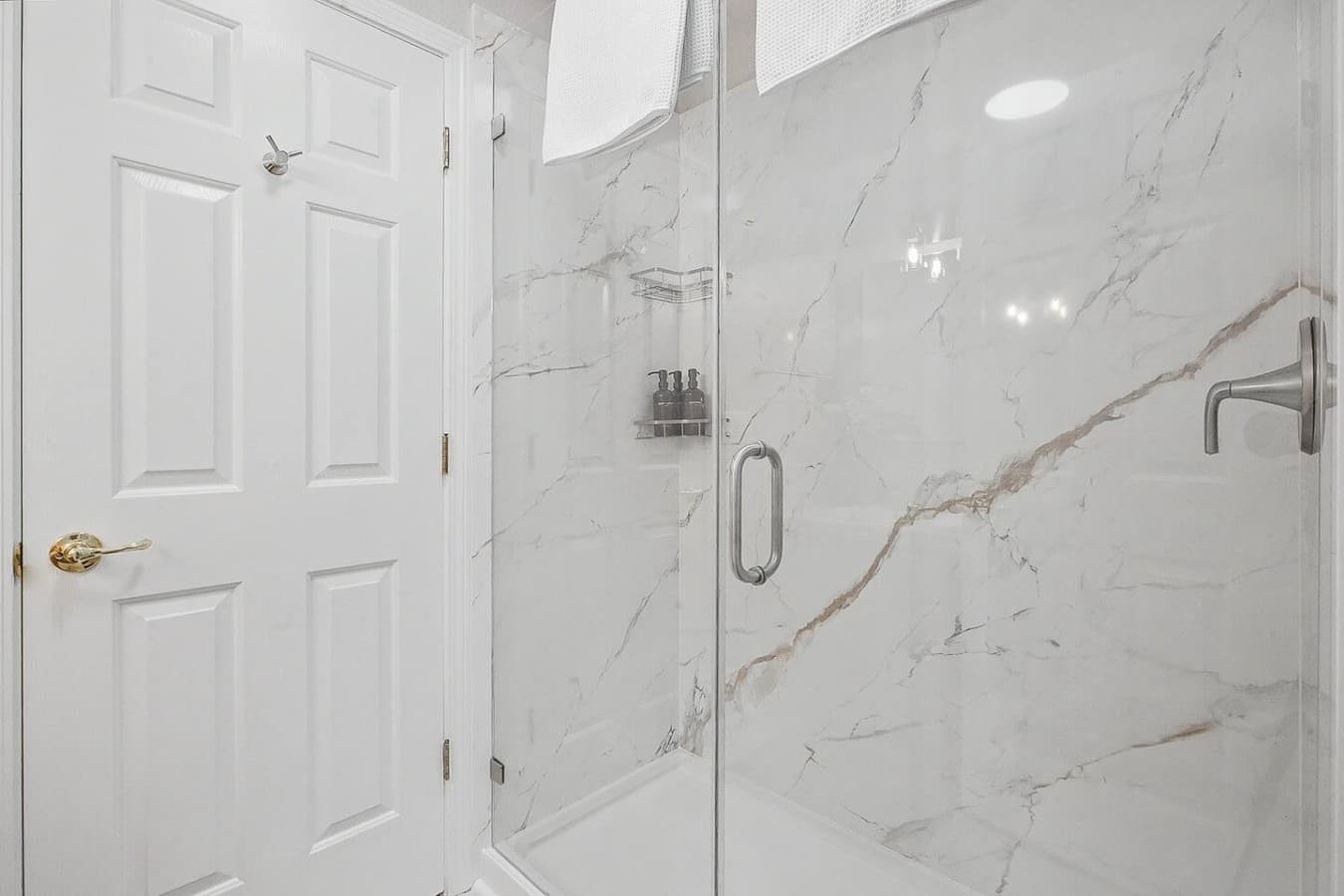 Sleek glass walk in shower with bright marble style tile and updated finishes.