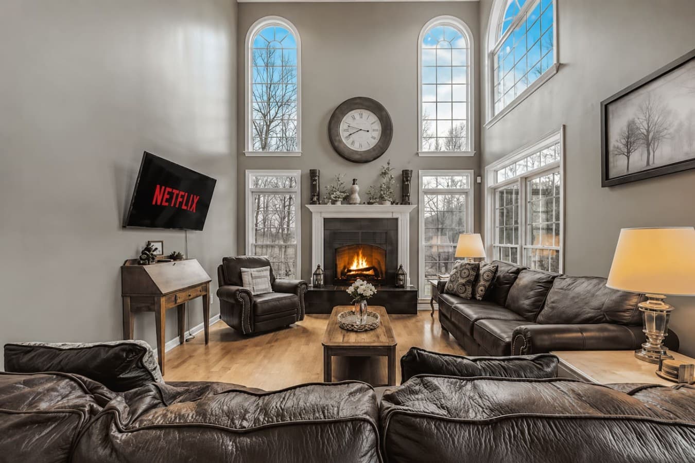 Grand living room with soaring ceilings, oversized windows, and a cozy stone fireplace.