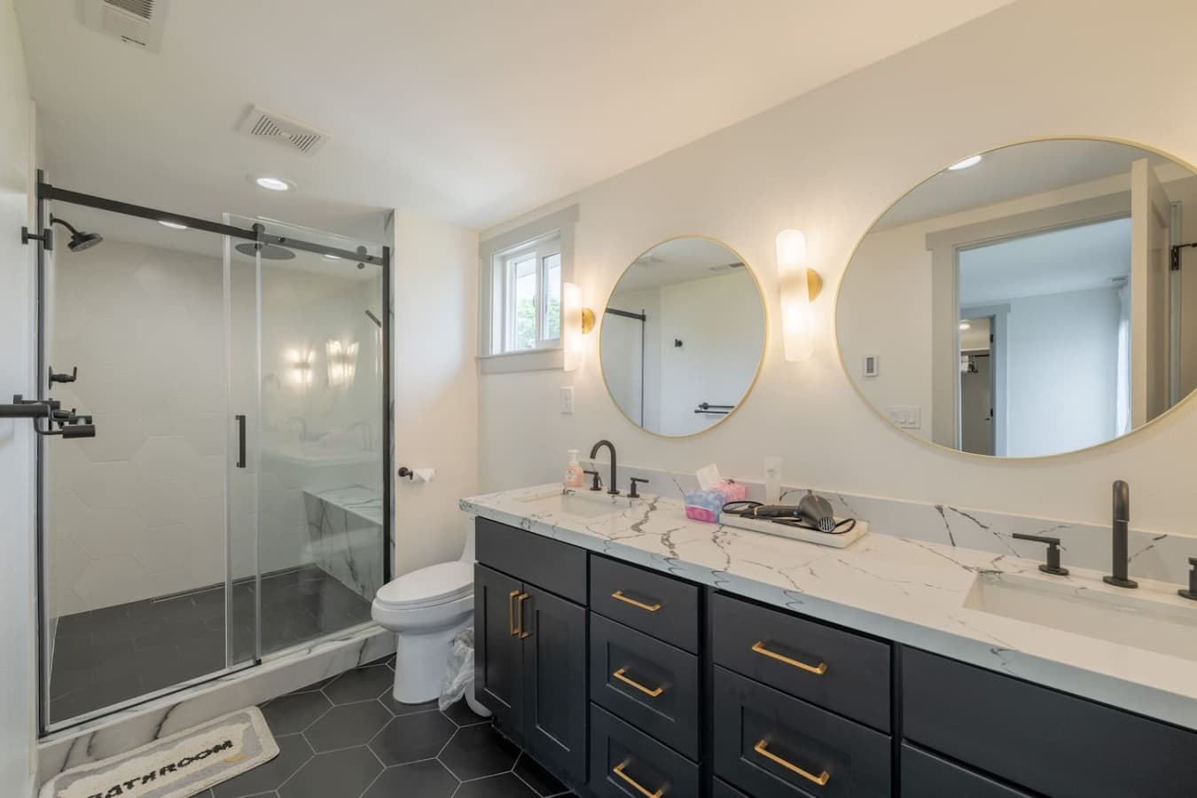 Bright and spacious bathroom featuring dual sinks, stylish lighting, and plenty of counter space for guests.