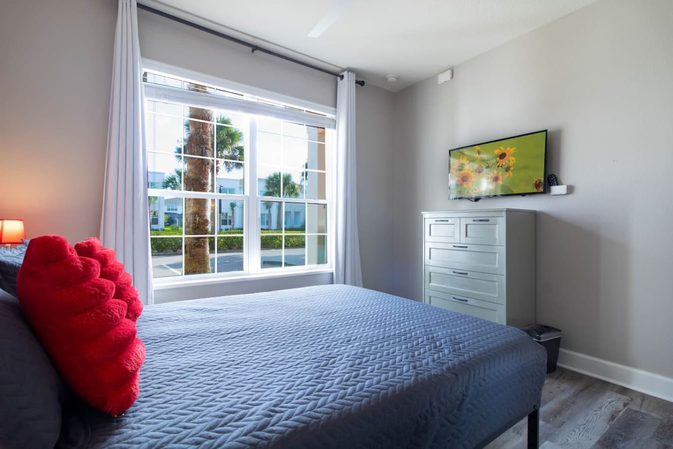 Comfortable bedroom with abundant natural light and a dresser with mounted television.