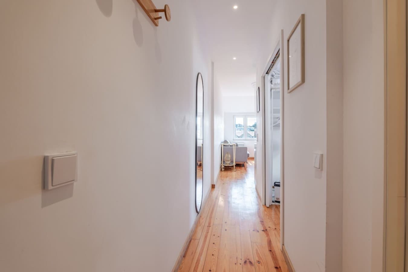 Long, light-filled hallway leading to the main living area with warm wooden flooring and a minimalist design.