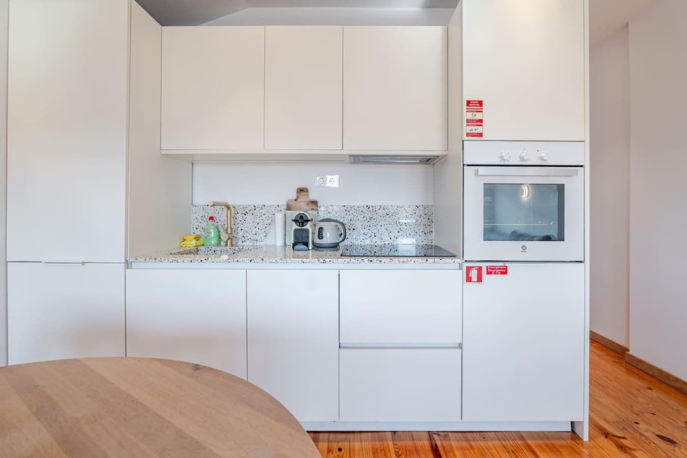 Fully equipped modern kitchenette with integrated appliances, terrazzo-style backsplash, coffee machine, kettle, and ample storage.