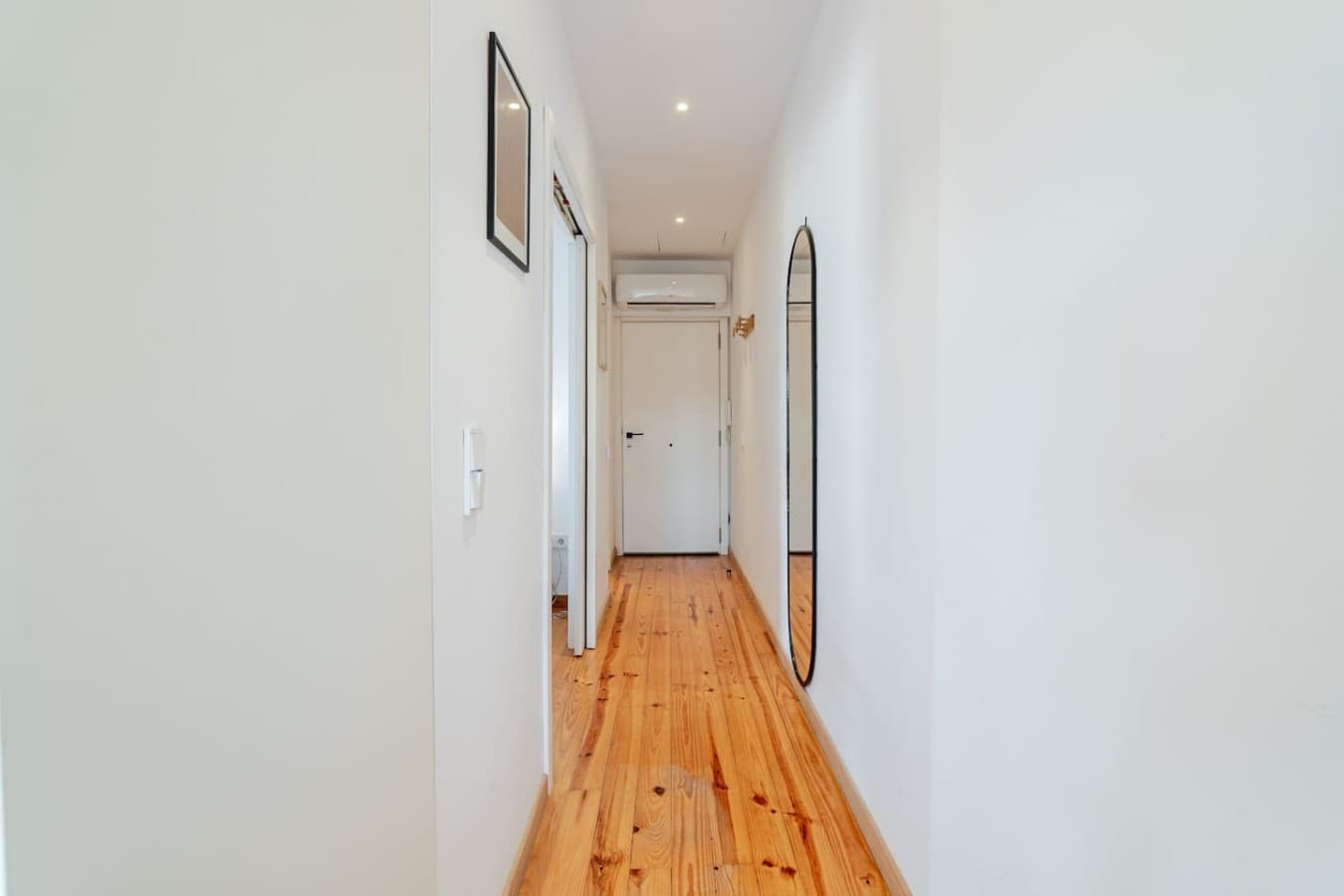 Bright entrance hallway with polished hardwood floors, recessed lighting, a full-length mirror, and air conditioning.