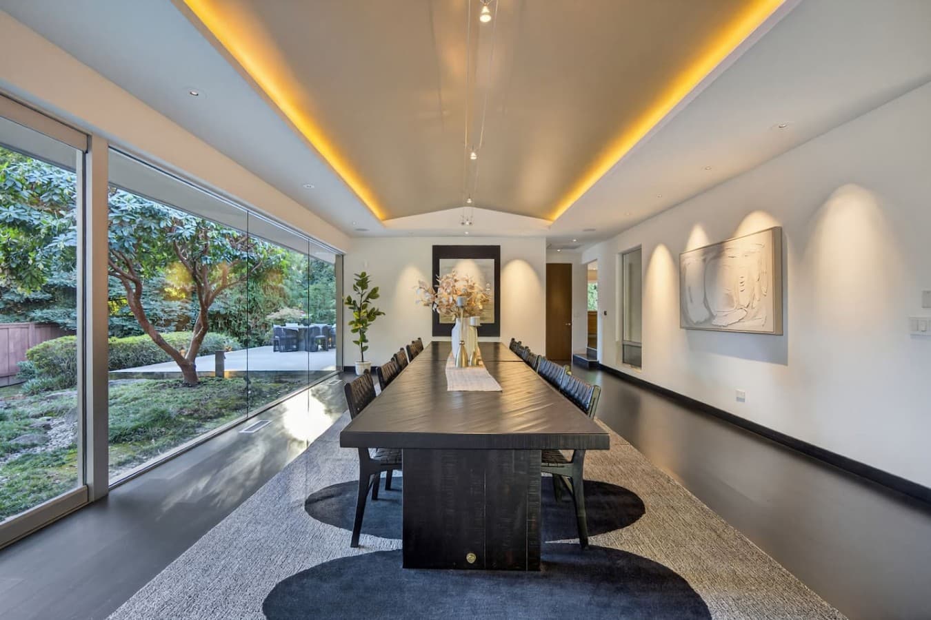 Formal dining room with seating for a crowd, dramatic lighting, and garden views through expansive windows.