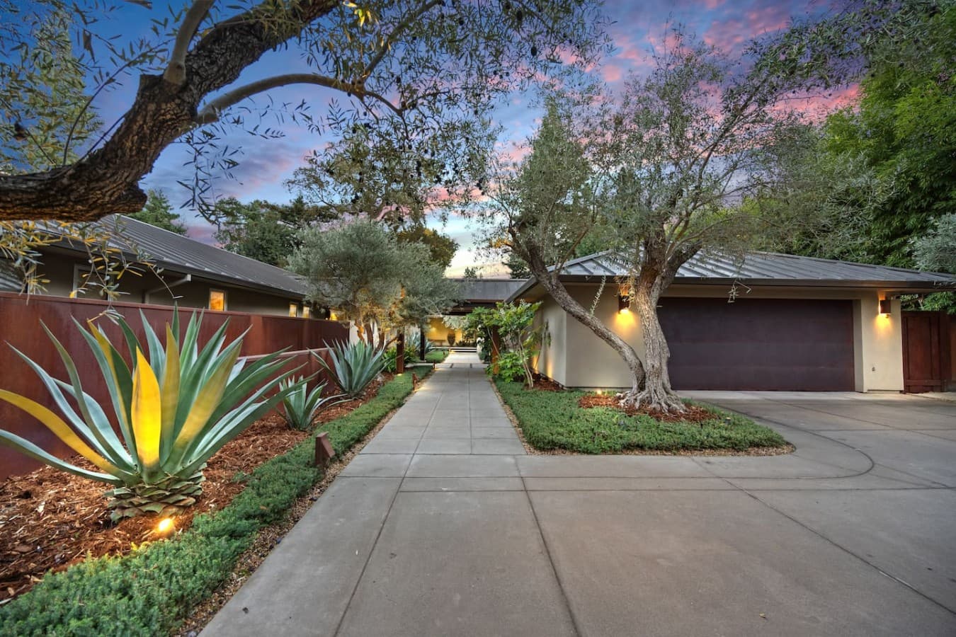 Gated driveway entrance framed by mature trees and thoughtfully designed gardens.