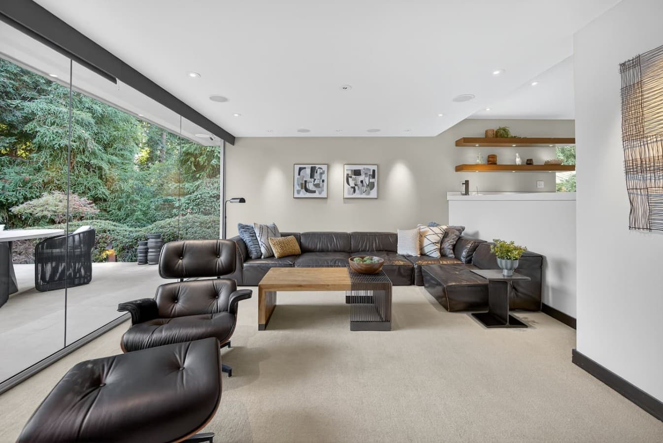 Sunlit living room with plush seating and serene forest views through expansive glass walls.