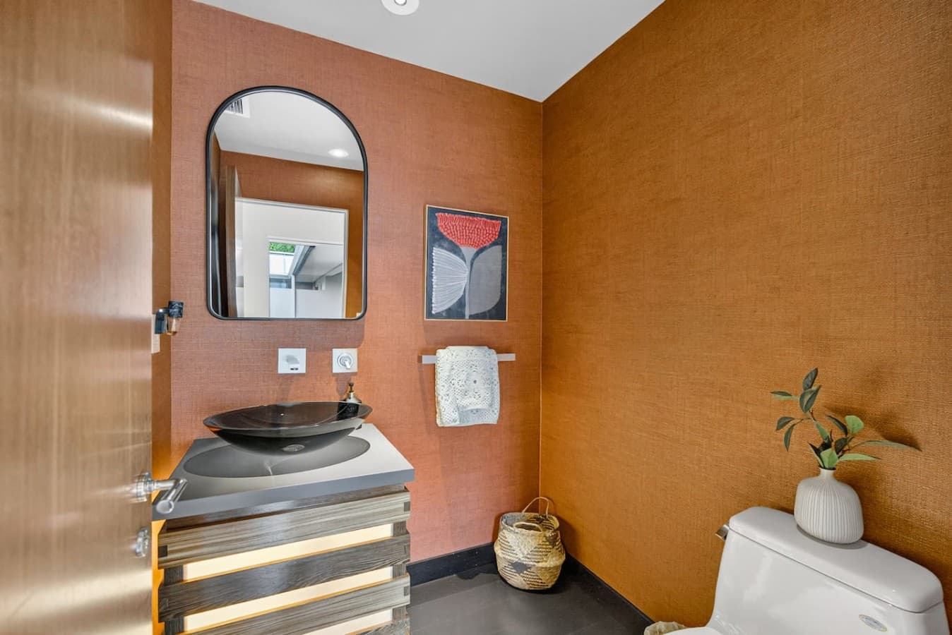 Designer powder room featuring a striking vessel sink, warm textured walls, and contemporary finishes.
