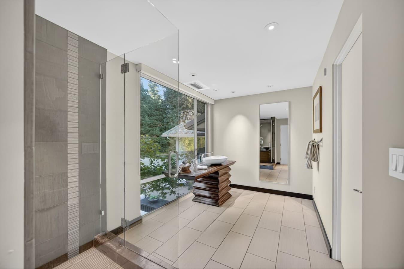 Bright spa inspired bath featuring a walk in glass shower, elegant finishes, and peaceful garden views.
