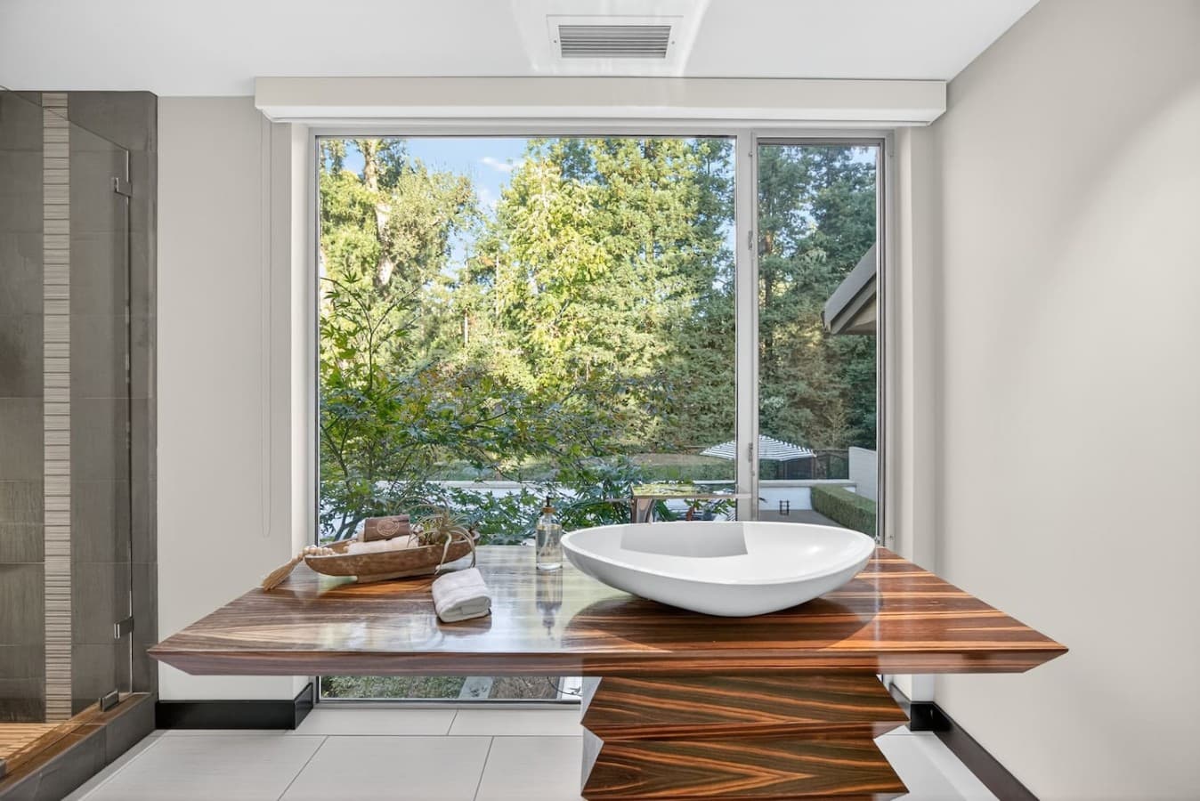 Serene bathroom retreat with a sculptural vessel sink and floor to ceiling windows overlooking lush greenery.