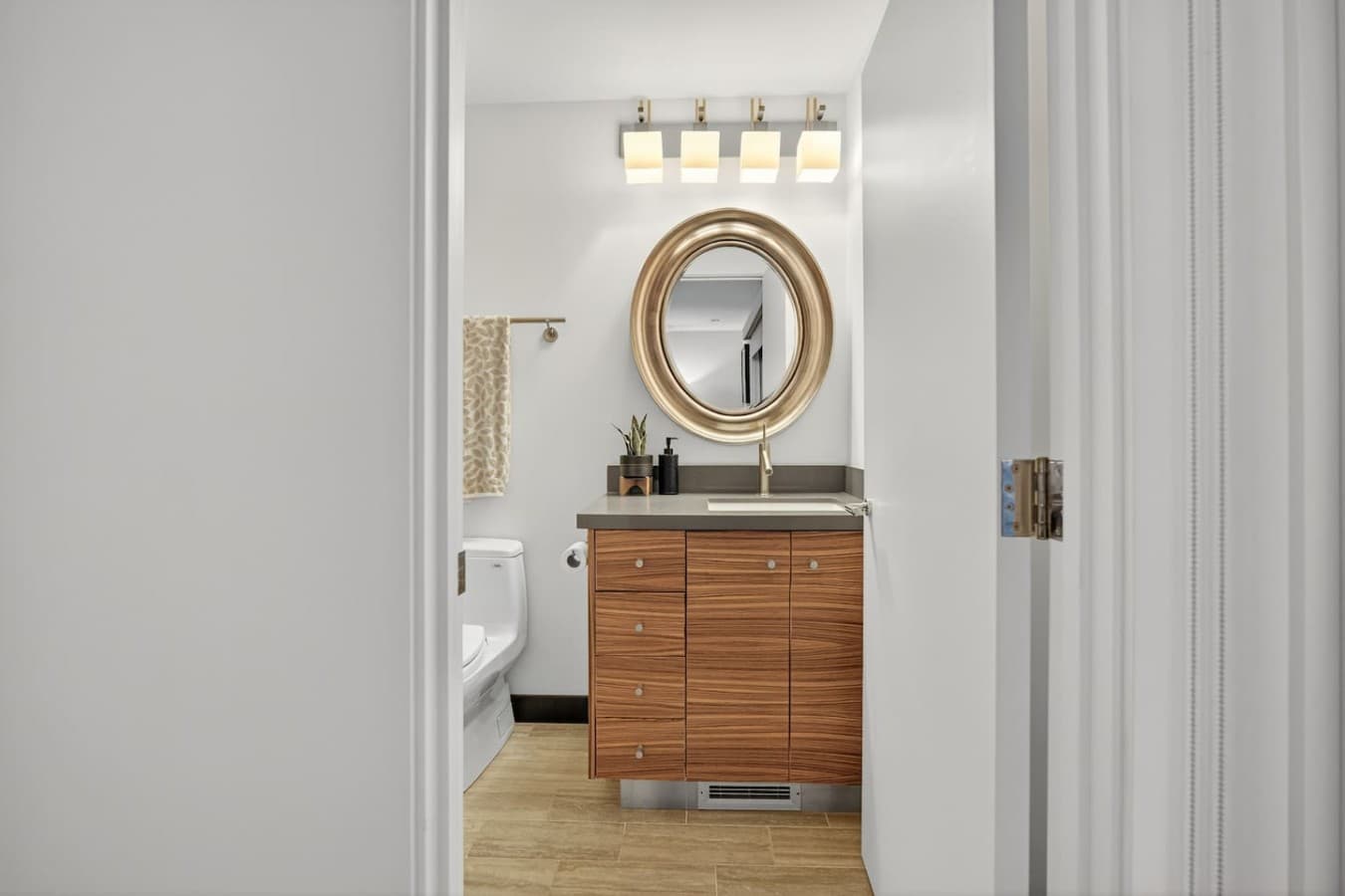 Stylish powder room featuring warm wood cabinetry, a statement mirror, and modern finishes.