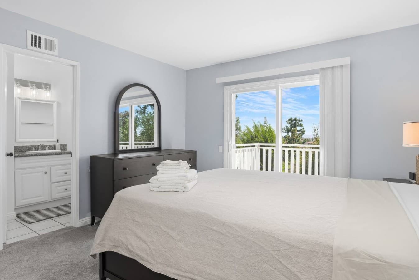 Bright upstairs bedroom with balcony access and peaceful neighborhood views.