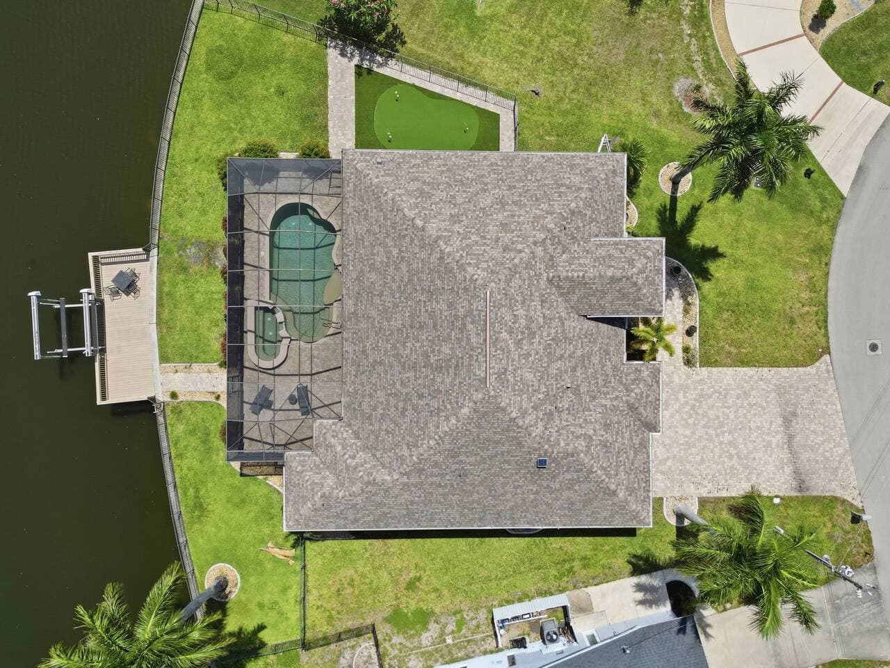 Birds eye view of the home featuring the screened pool area, dock, and backyard putting green.