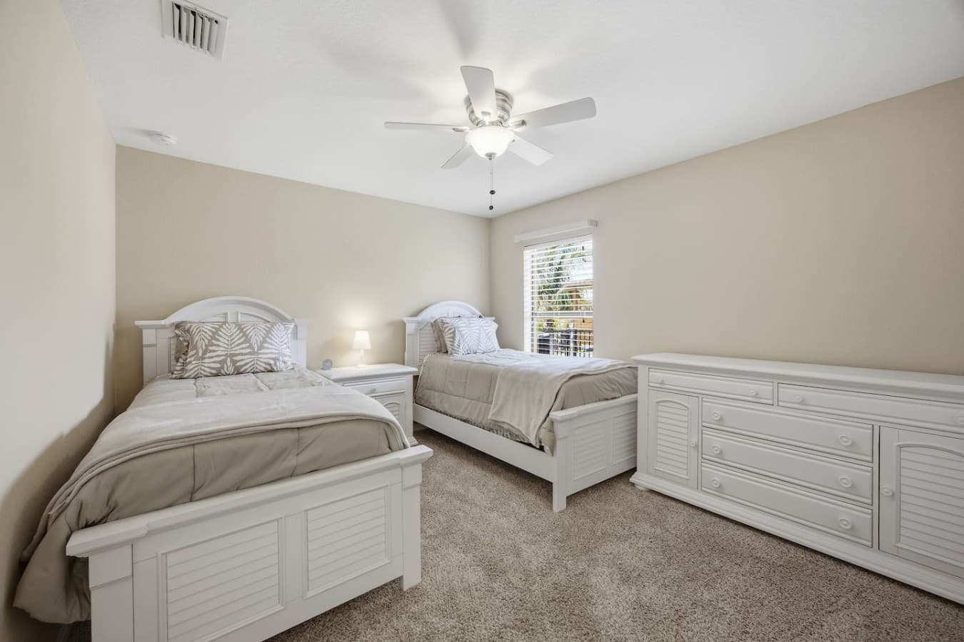 Bright guest bedroom with two twin beds, plush carpeting, and a ceiling fan.