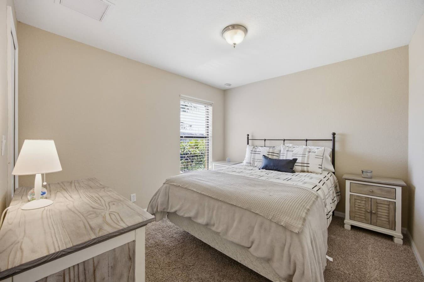 Cozy guest bedroom with soft natural light, plush carpeting, and comfortable furnishings.