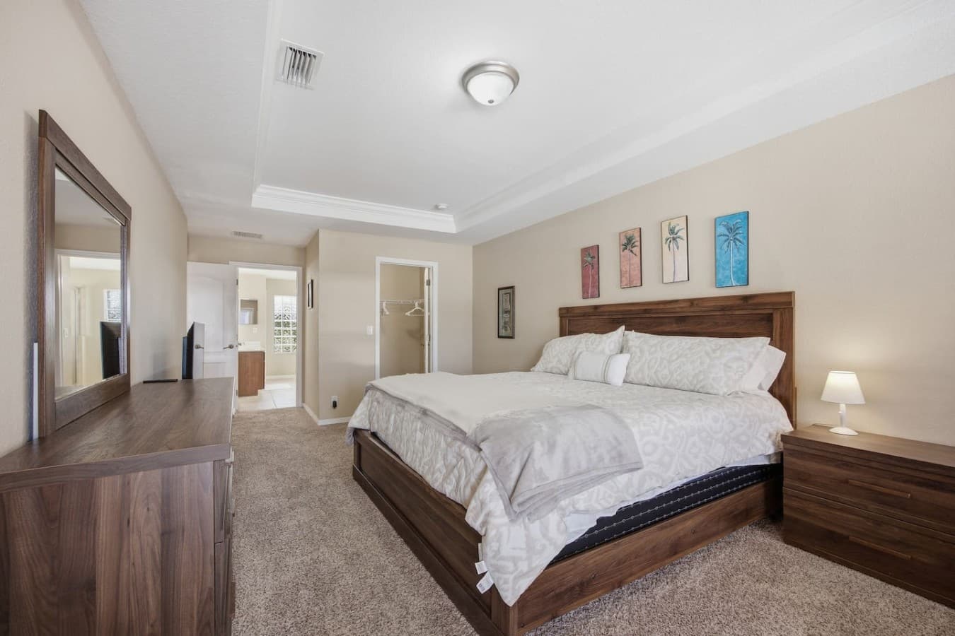 Spacious primary bedroom with a tray ceiling, plush carpeting, and elegant furnishings.