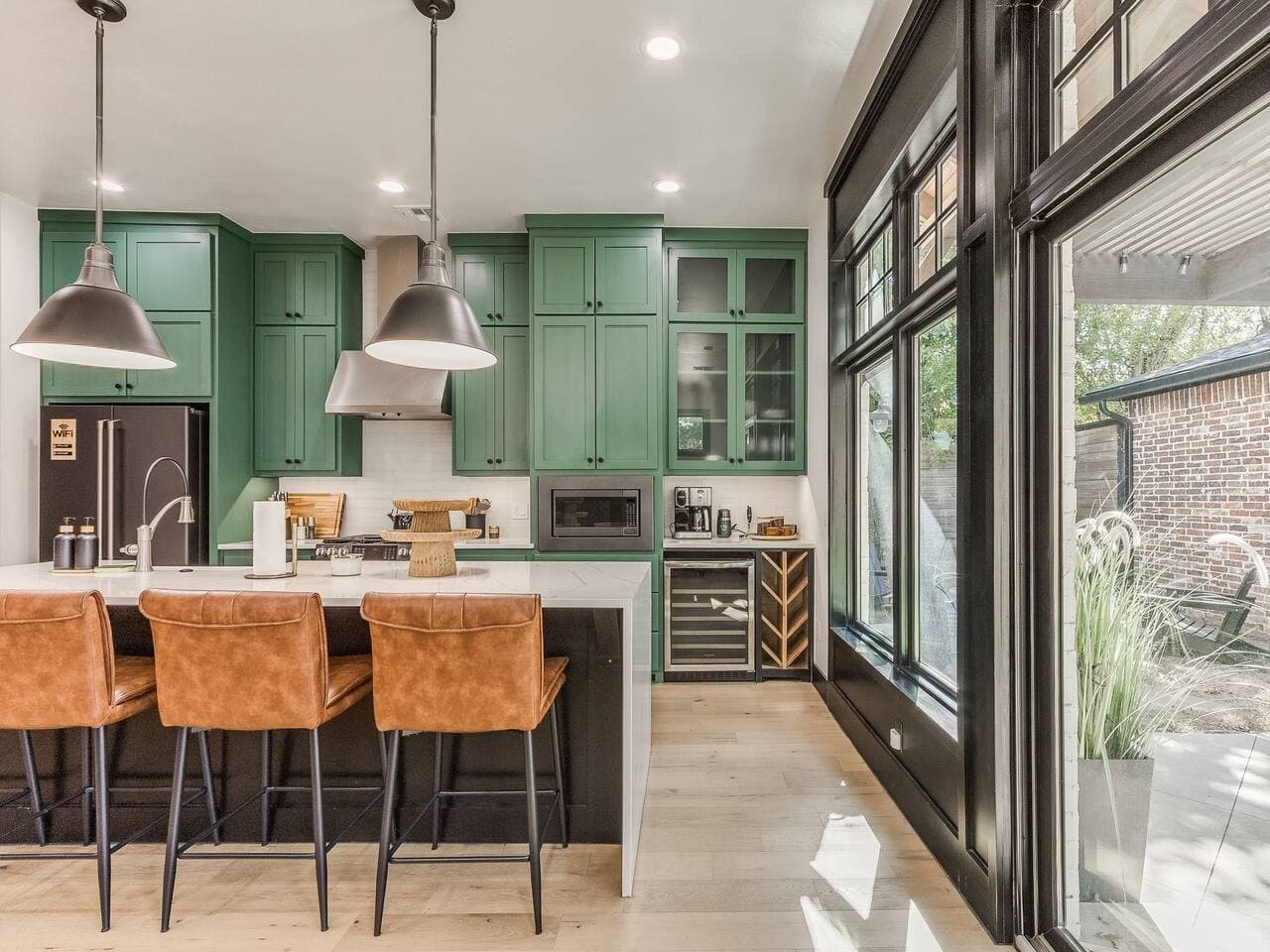 Bright designer kitchen with striking green cabinetry, bar seating, and floor to ceiling windows.