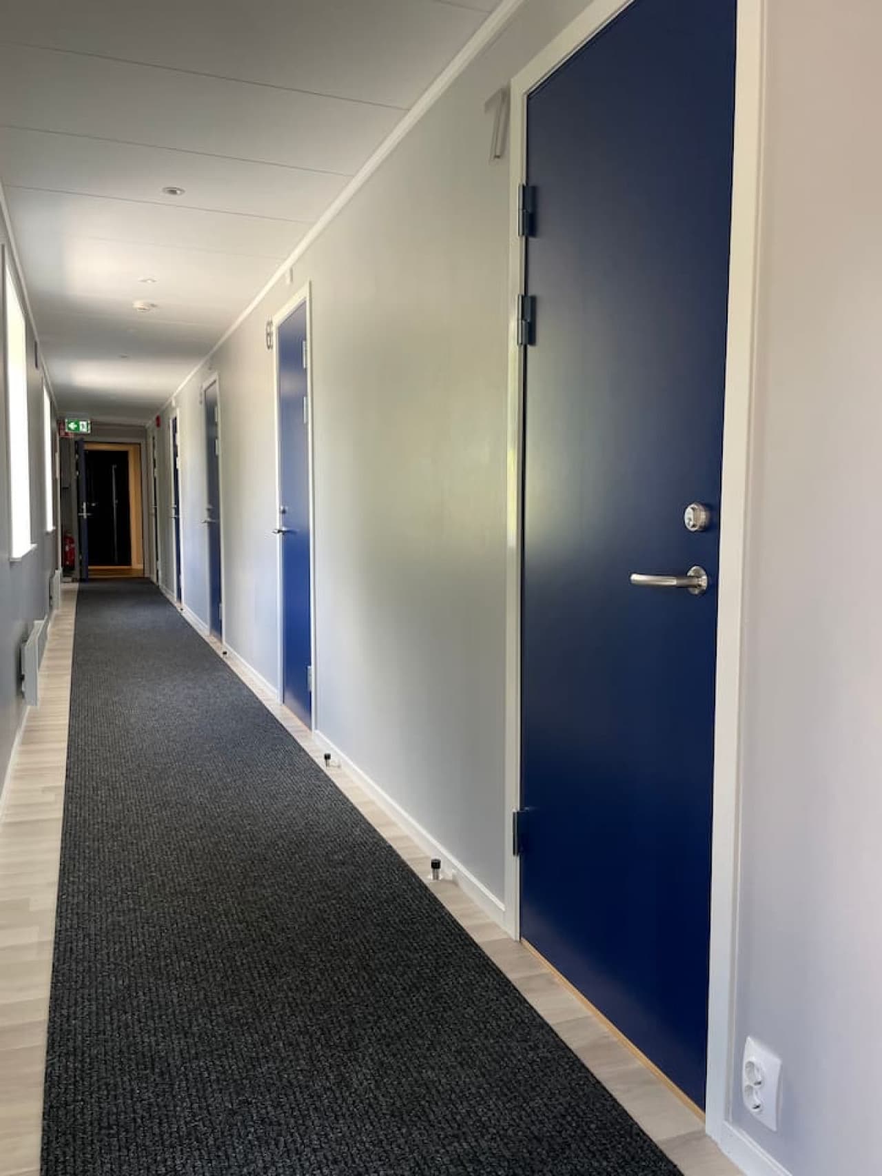 Hallway in lakefront building with doors to five identical bedrooms with bunk beds. Each bedroom sleeps 6 persons.