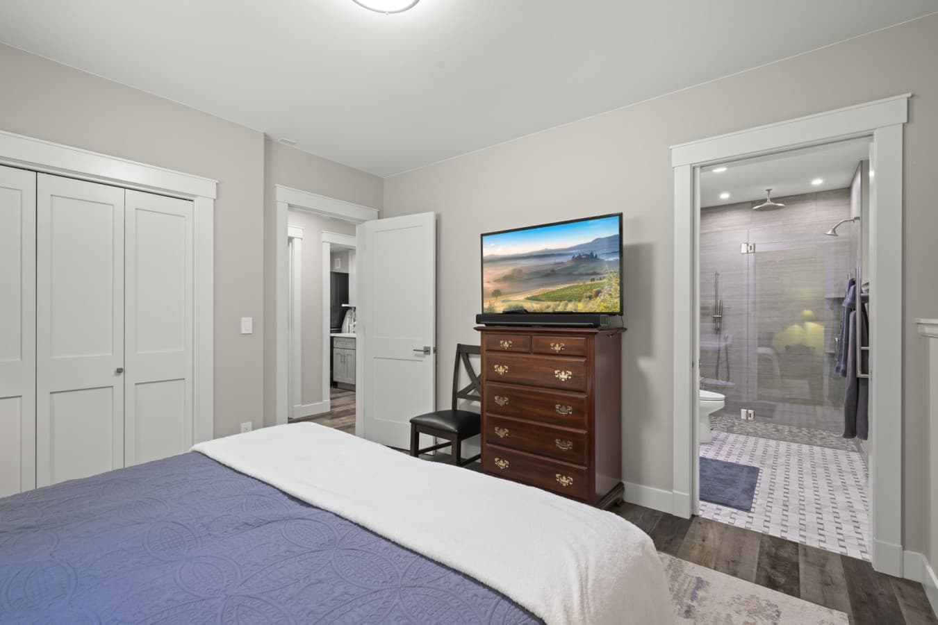 Primary bedroom featuring a queen-size bed, Smart TV, dresser, and direct access to the ensuite bathroom_.jpg