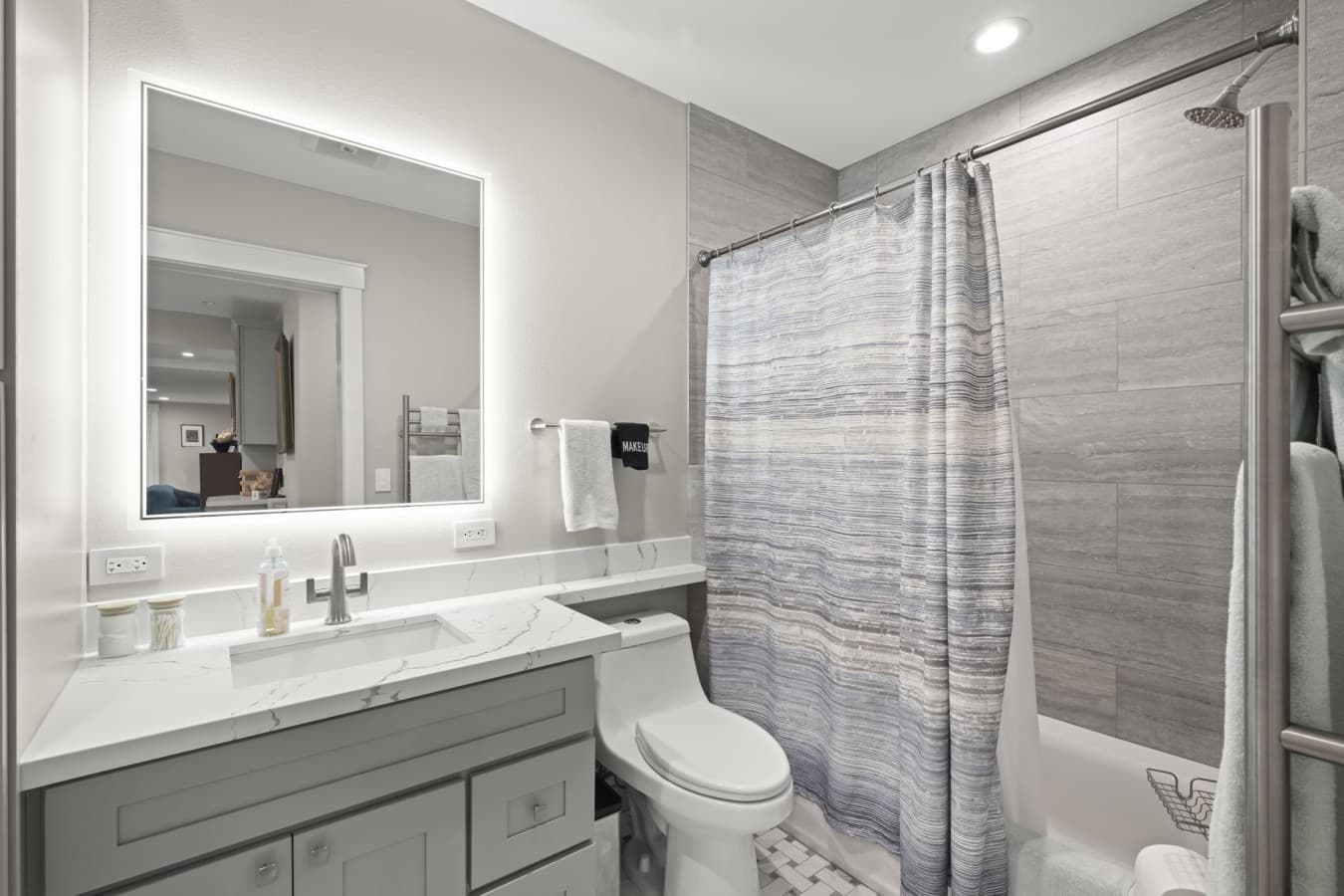 Full guest bathroom with a vanity, illuminated mirror, toilet, and shower-and-tub combination_.jpg