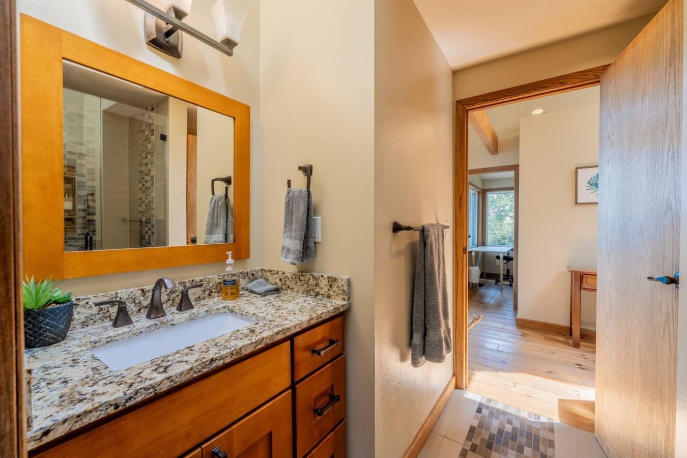 A bright, well-appointed bathroom featuring a granite vanity, warm wood finishes, and a spacious walk-in shower.