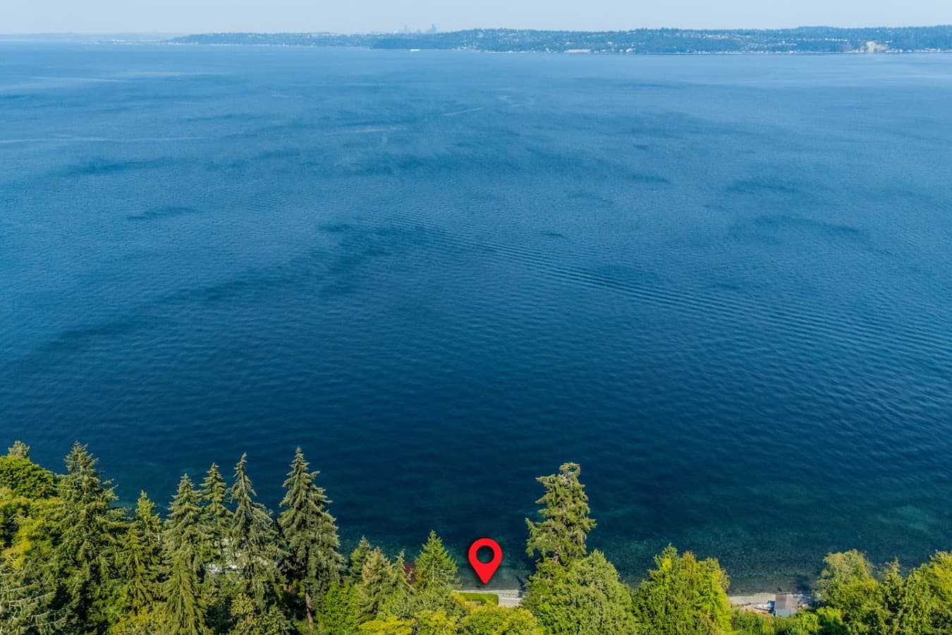 A truly waterfront escape—surrounded by lush greenery with the shoreline just steps away and endless blue-water views stretching toward the horizon.