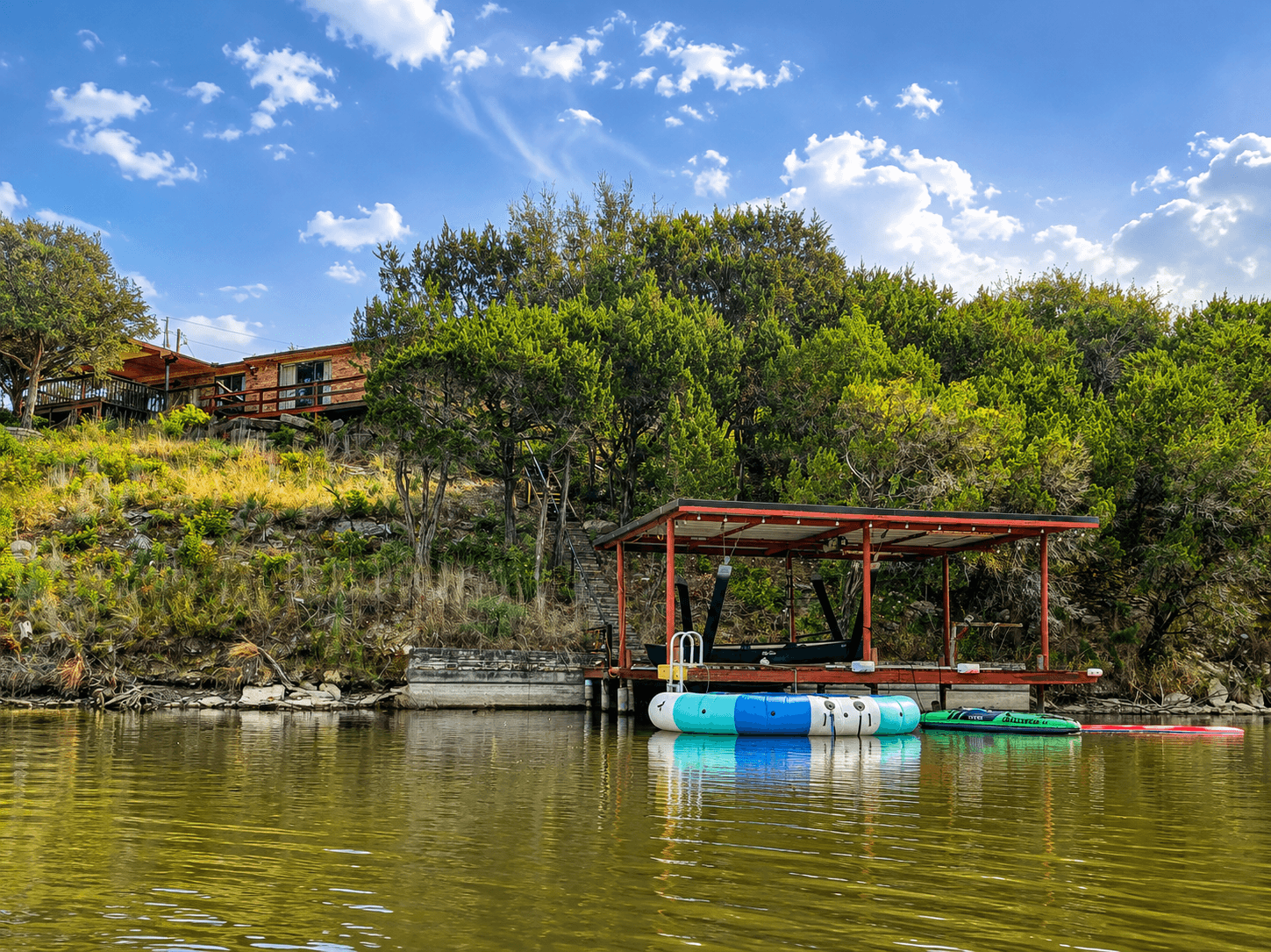Private lakefront dock stocked for fun on the water, with life jackets, an inflatable trampoline, lily pad, inflatable kayak, canoe, and assorted inflatable tubes.