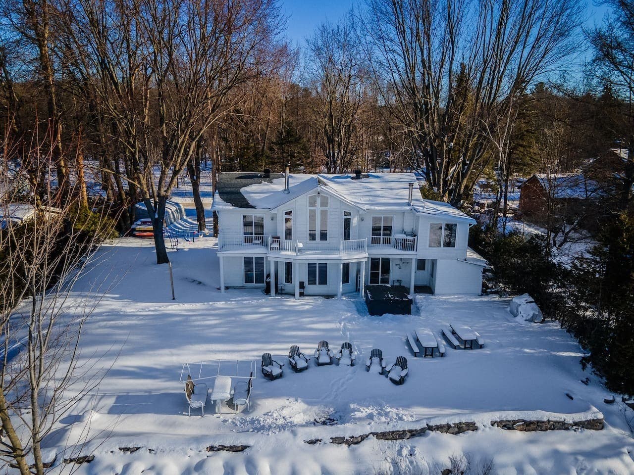 Chalet au bord de la rivière des Outaouais avec spa privé et foyer extérieur entouré de chaises, idéal pour se détendre en famille ou entre amis tout en profitant de la vue sur l’eau