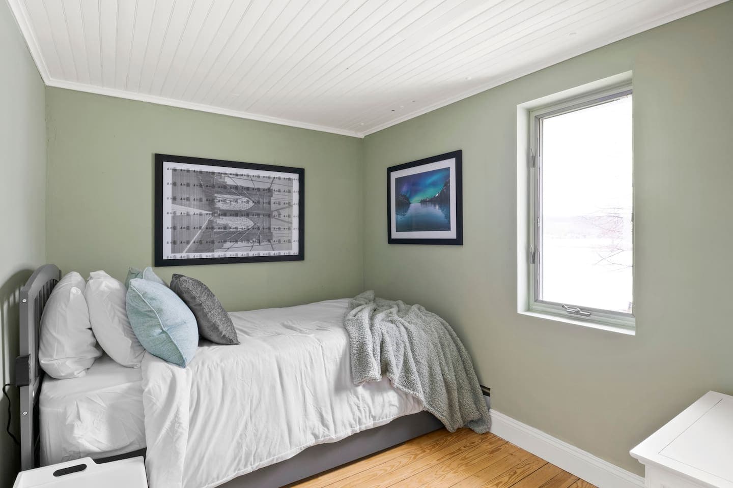 Green bedroom with a grey bed and framed artwork
