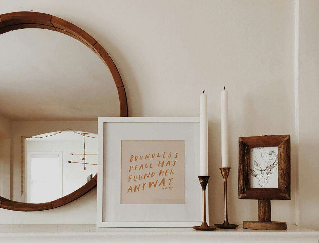 A mirror, framed prints, and candle sticks on a mantle.